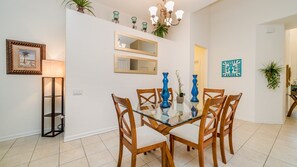A dining area with a glass table, wooden chairs, and a chandelier. - Windsor Hills Resort 5 Bedroom Private Pool+Spa Home (Kissimmee)