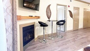 A hotel room with a flat-screen TV mounted on the wall, a fireplace, and two bar stools. - Sweet Drake - Unit 2103 - FREE Attraction Ticket with EACH night Stay Including Dollywood (Pigeon Forge)