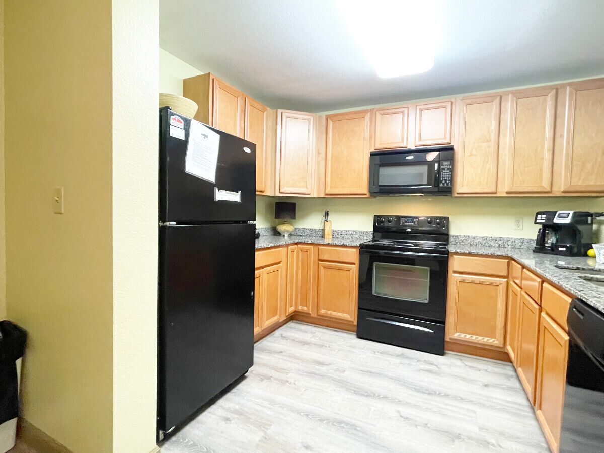 A kitchen with wooden cabinets, a black refrigerator, a microwave, an oven, and a dishwasher.