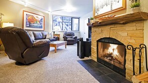 Ein Wohnzimmer mit Kamin aus Stein, Ledersofas, einem Couchtisch und einem großen Fenster.