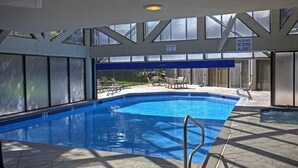 Ein Hallenbad mit klarem, blauen Wasser, einem blauen Sicherheitszaun und einem Schild, das auf flaches Wasser hinweist und das Tauchen untersagt.