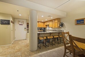 A kitchen with wooden cabinets, a bar area with stools, a refrigerator, and a microwave.