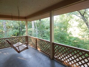 A covered porch with a swing, wooden lattice railings, and a view of a forested area.