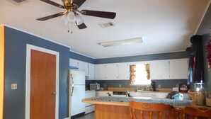 Une cuisine avec des armoires blanches, un îlot central en bois et un ventilateur de plafond.
