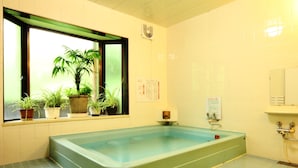 A bathroom with a large bathtub, a window with plants, and a tiled floor. - Yokokura-inn (Nagano)