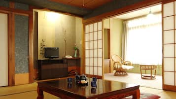 A traditional Japanese room with tatami flooring, a low wooden table, a television, and a sliding door leading to another room.