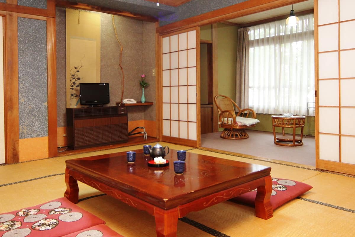 A traditional Japanese room with tatami flooring, a wooden table with cups and a teapot, a television, and a sliding door leading to another room.