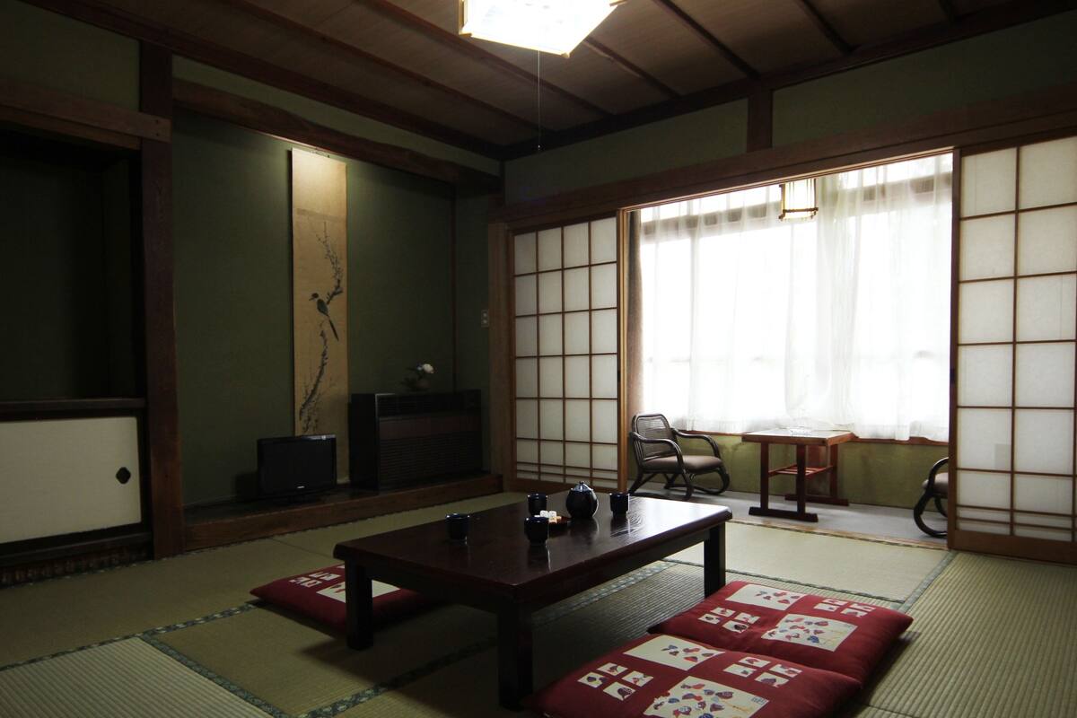 A traditional Japanese room with tatami flooring, a low table, a chair, and sliding shoji doors.