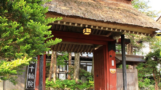 A traditional Japanese building with a thatched roof, wooden pillars, and a stone pathway leading to the entrance. - Yokokura-inn (Nagano)