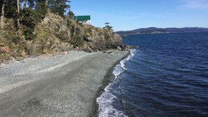 Una strada costiera con un litorale roccioso, un edificio verde su una scogliera e vista sull'oceano e colline lontane.