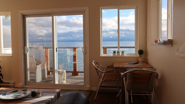 Una stanza con vista sul mare, una zona pranzo con sedie e tavolo, e una porta scorrevole in vetro che dà su un terrazzo.