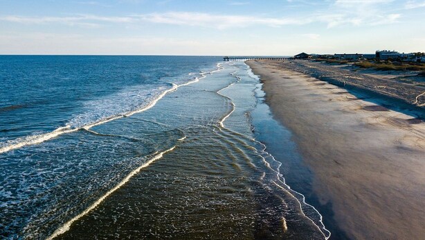 A beach with a long pier extending into the sea, a sandy shoreline, and buildings in the background. - Best Located Vacation Rental on all of Tybee Island (Tybee Island)