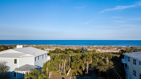 A coastal residential area with a view of the ocean, featuring modern houses, a beach, and a clear sky.