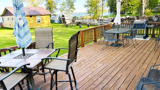Une terrasse en bois avec des sièges d’extérieur, un barbecue et une vue sur un lac.