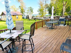 Une terrasse en bois avec des sièges d’extérieur, un barbecue et une vue sur un lac.