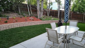 A patio with a round table and chairs, a stone retaining wall, and a wooden fence in the background.
