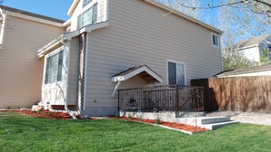 A two-story house with a covered porch, a small front yard with a lawn and mulch, and a wooden fence in the background.