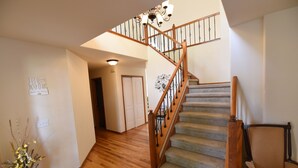 A staircase with wooden railings and carpeted steps leading to a landing. A vase with dried flowers is on the floor beside the stairs.