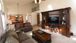 A spacious living room with a large wooden entertainment center, a ceiling fan, and a kitchen in the background.