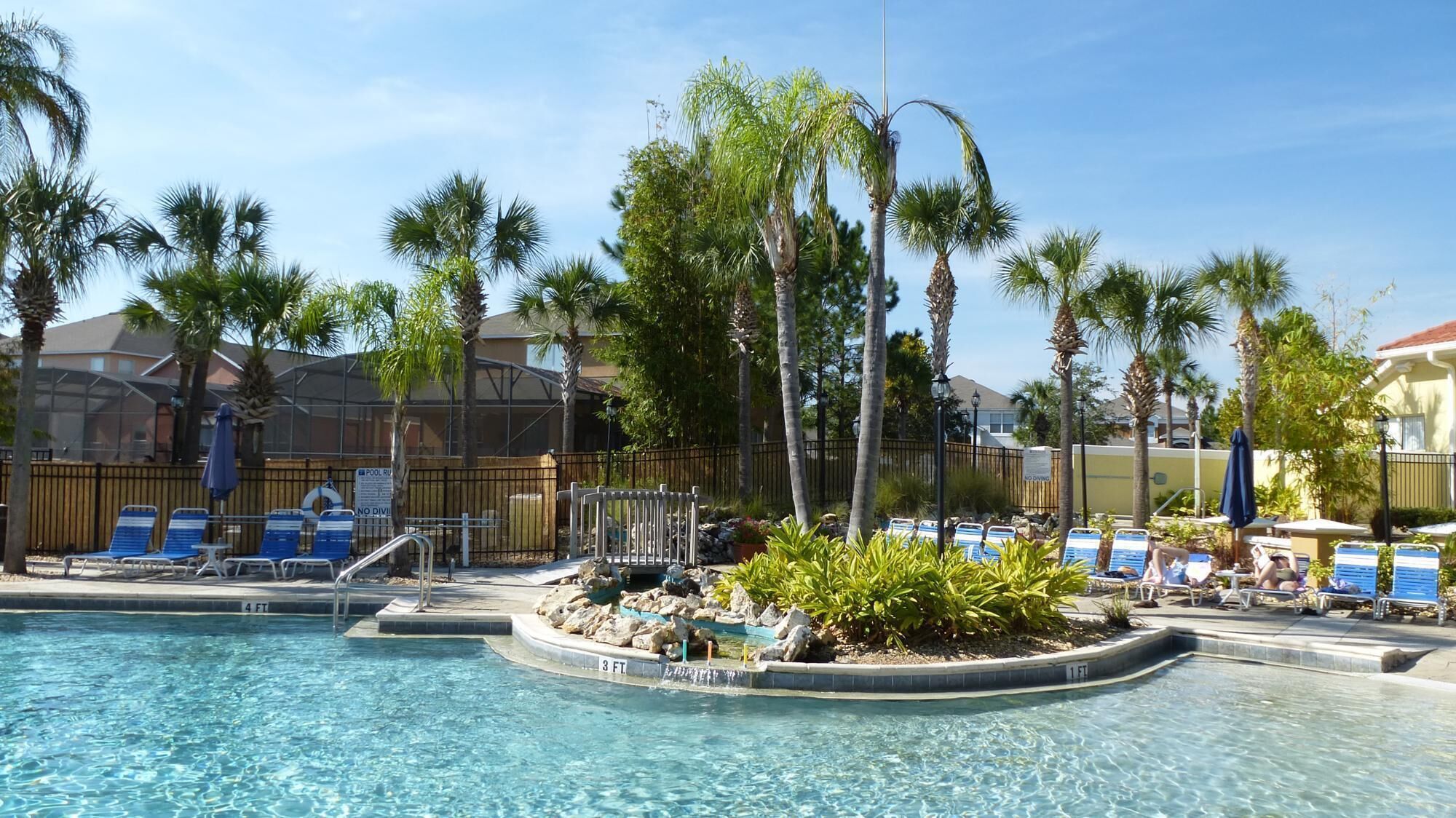 A pool area with lounge chairs, palm trees, and a wooden fence.