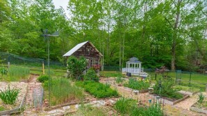 A rustic wooden cabin with a small shed, surrounded by a garden with raised beds and a stone pathway.