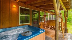 A wooden cabin with a hot tub, wooden deck, and a view of greenery.