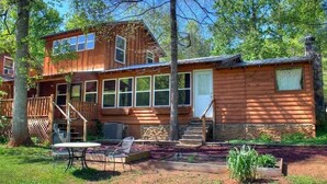 A two-story log cabin with a deck, a front porch, and a small outdoor seating area.