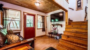 A wooden interior with a red door, a staircase, and a flat-screen TV mounted on the wall.