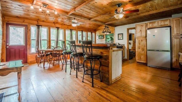 A wooden interior with a kitchen area, bar stools, and a refrigerator.