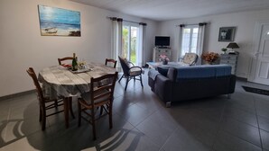 Un coin repas avec une table et des chaises en bois, un canapé, un téléviseur et une fenêtre avec des rideaux.