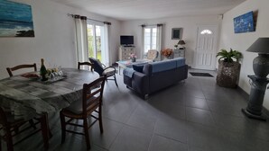 Il y a un coin repas avec une table, des chaises et un téléviseur. Le salon est équipé d’un canapé et d’une lampe.
