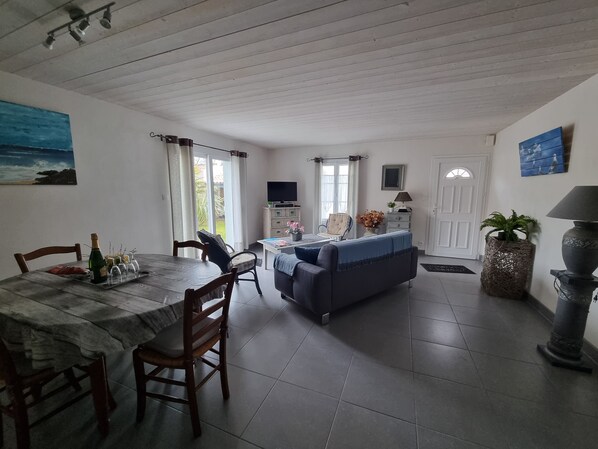 A dining area with a table, chairs, and a TV. There is a sofa and a lamp in the living area.