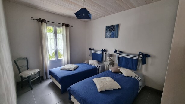 Une chambre avec deux lits, une chaise, une fenêtre avec des rideaux et un luminaire au plafond.