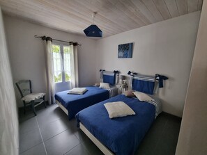 A bedroom with two beds, a chair, a window with curtains, and a ceiling light fixture.