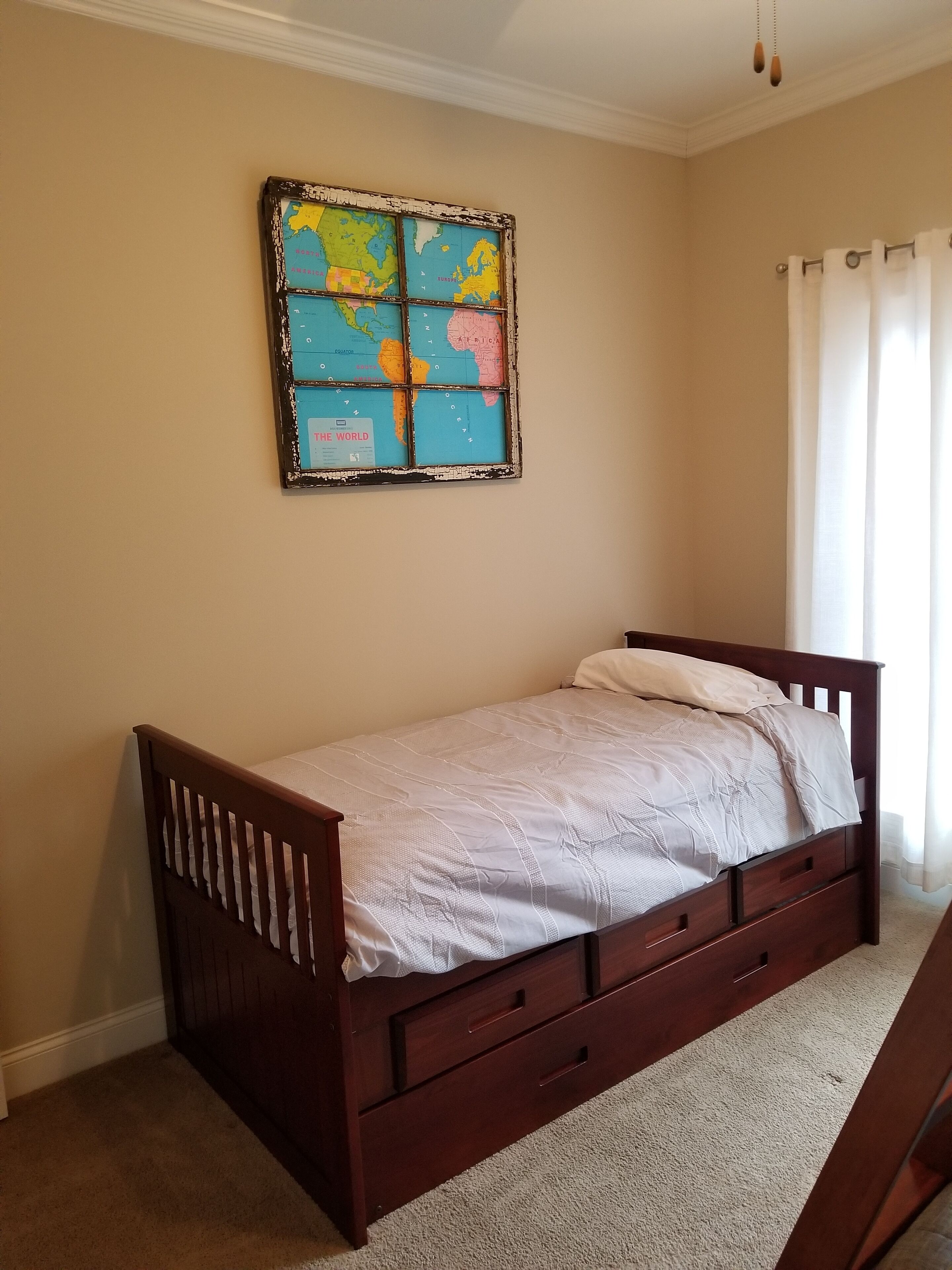 A bedroom with a wooden bed, a world map on the wall, and a window with curtains.