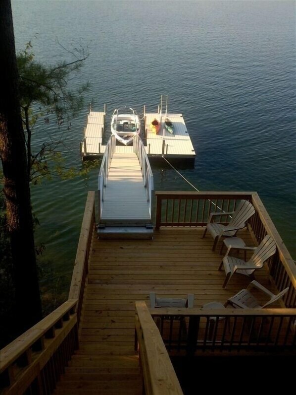 Guests can enjoy serene waterfront views from the deck, featuring Adirondack chairs and a small boat.