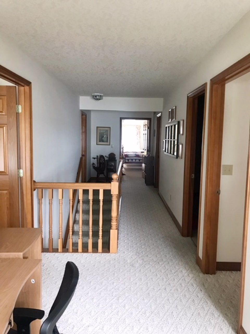 A hallway with a wooden staircase, carpeted floors, and a door on the left.