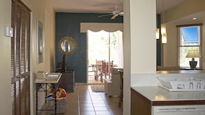 A well-lit hallway with a ceiling fan, a dining area with chairs and a table, and a kitchen area with a refrigerator and a lamp. - pvCouple Escape, Spacious, Close to Dining, Tennis, Poolside, & Near to Beach (Humacao)