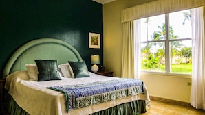 A bedroom with a large bed, a nightstand, a lamp, and a window with a view of greenery. - pvCouple Escape, Spacious, Close to Dining, Tennis, Poolside, & Near to Beach (Humacao)