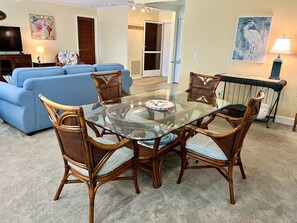 Un salon avec un canapé bleu, une table à manger en verre entourée de chaises en osier et un téléviseur posé sur un meuble.