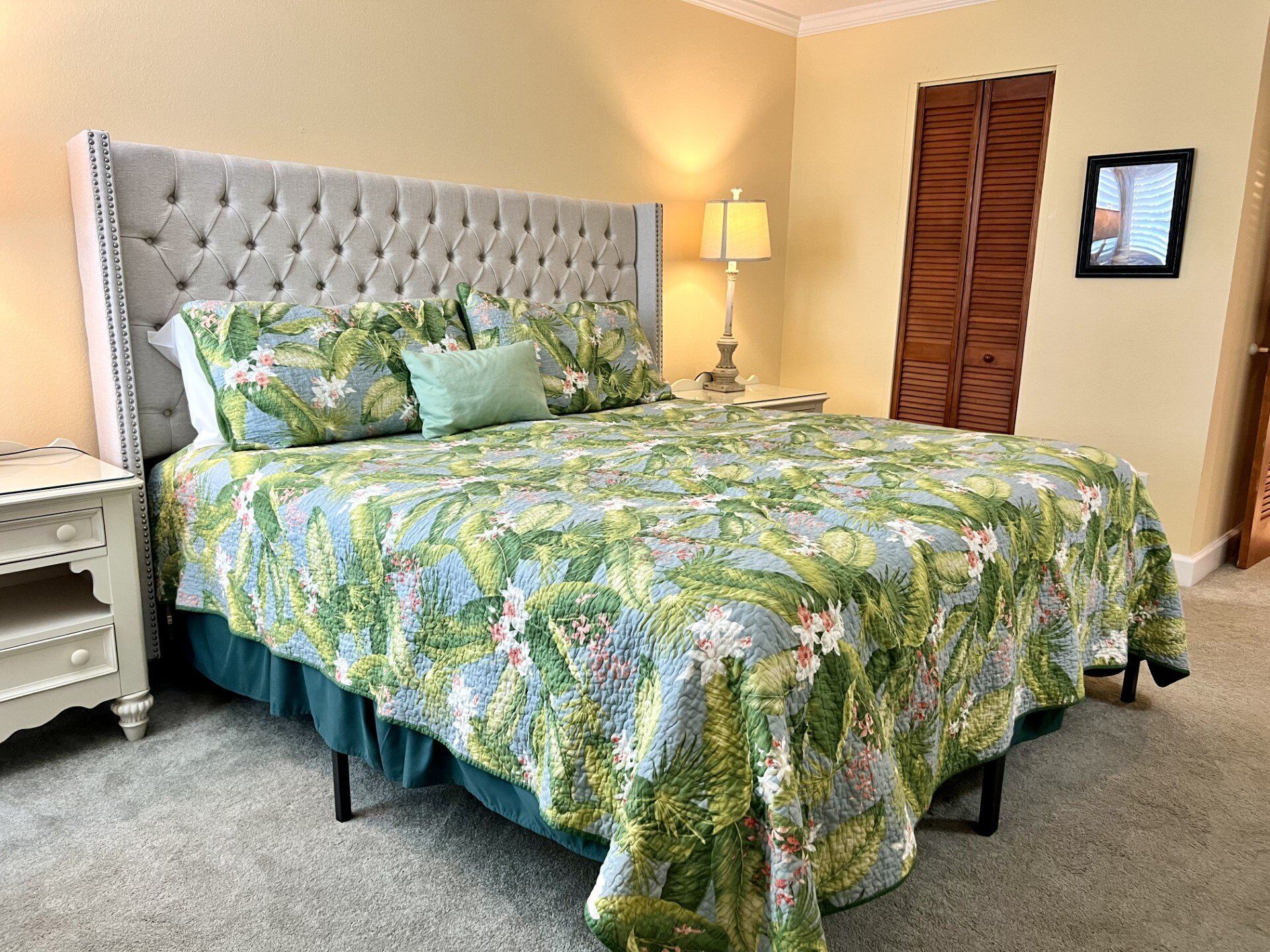 Quarto com cabeceira estofada, roupa de cama floral, mesa de cabeceira com abajur e armário de madeira.