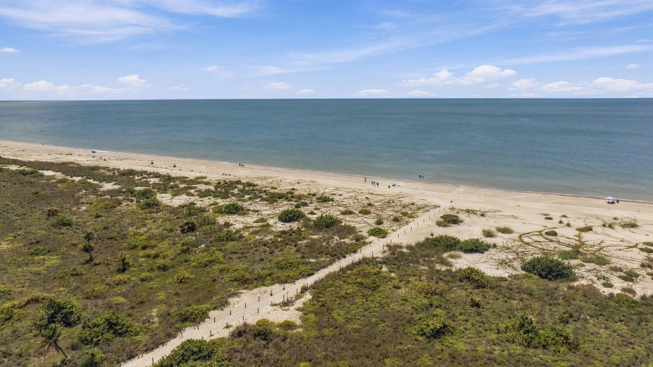 A beach with a clear view of the ocean, sandy terrain, and sparse vegetation.