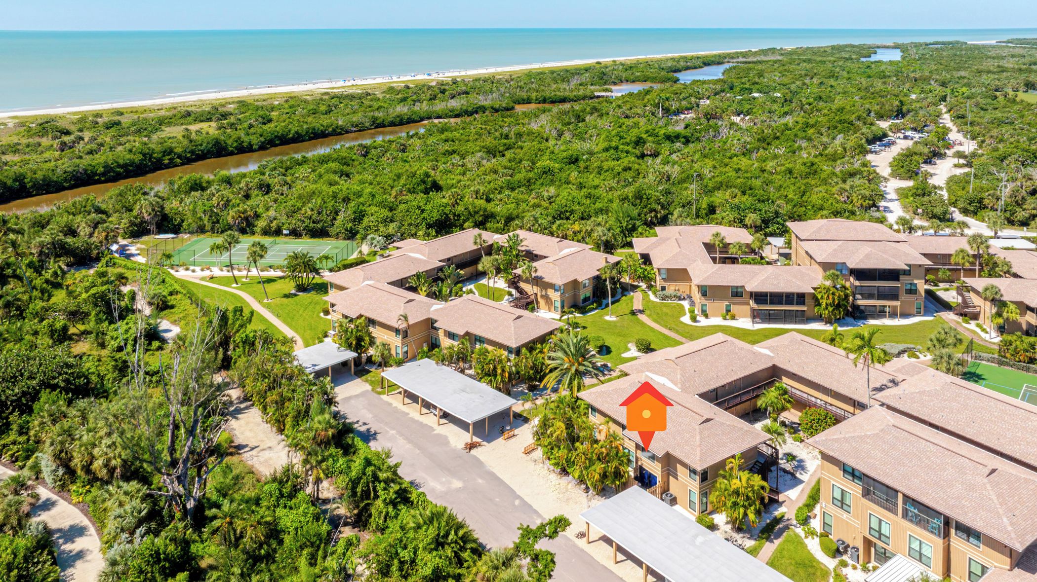 A residential area with multiple two-story buildings, a tennis court, and a beachfront view.