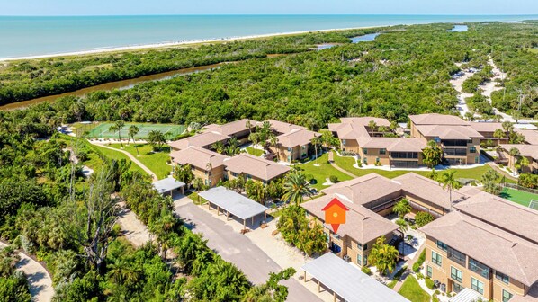 A residential area with multiple two-story buildings, a tennis court, and a beachfront view.