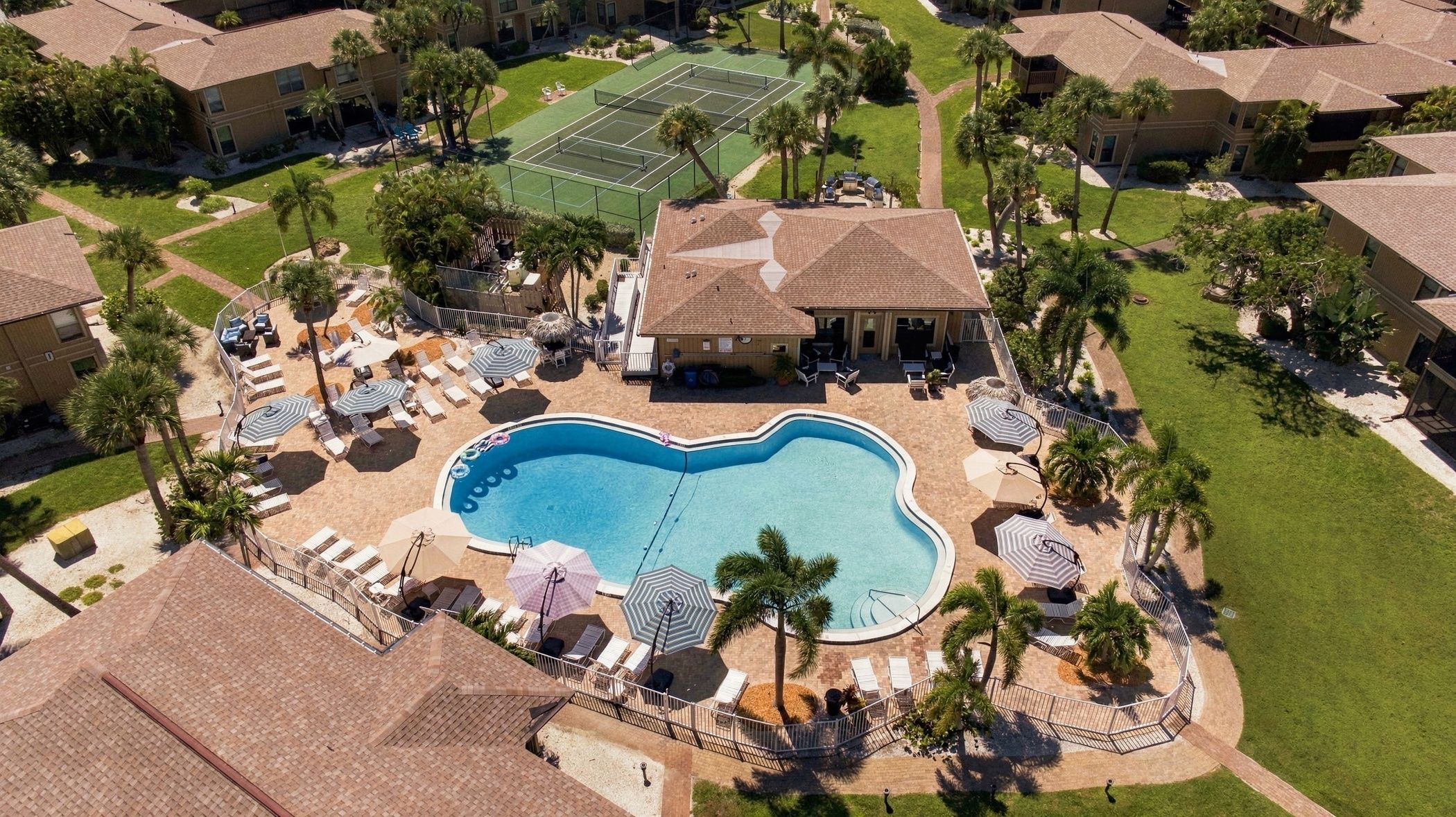 A residential area with a swimming pool, lounge chairs, and a tennis court.