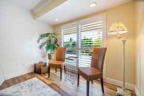 A room with two wicker chairs, a small table, a floor lamp, a potted plant, and a window with blinds.