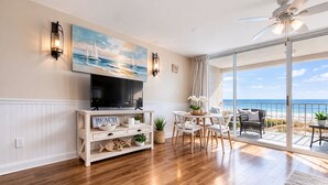 Ein Wohnzimmer mit Fernseher, einem Holz-TV-Schrank und einem Essbereich mit Blick auf den Strand.