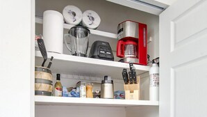 Een keukenkast met planken, gevuld met keukengerei, een koffiezetapparaat en opbergcontainers.
