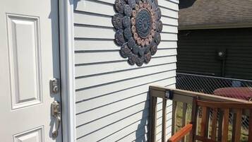 Uma porta branca com fechadura digital, um detalhe metálico decorativo na parede e um banco de madeira em um alpendre.