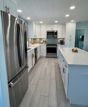 A modern kitchen with white cabinetry, stainless steel appliances, and a light-colored tile floor.